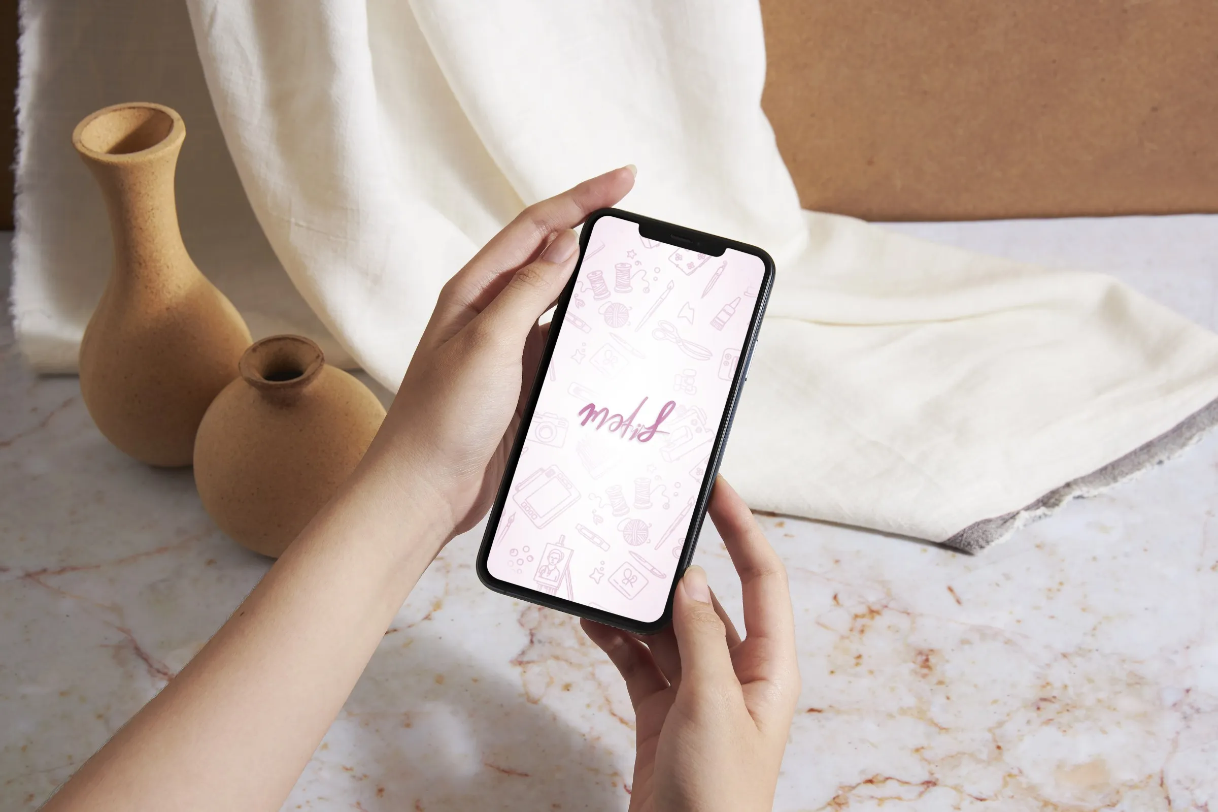A hand holding a phone showing the Motif splash screen, beside clay vases on a cream cloth.